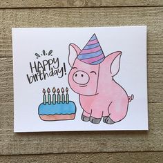 a pink pig with a birthday hat standing next to a cake on a wooden surface