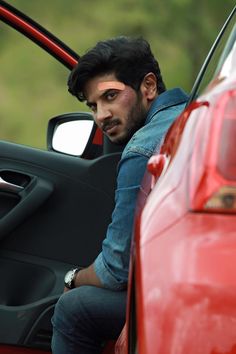 a man sitting in the driver's seat of a red car with his hand on the door handle