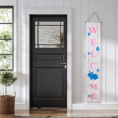 a welcome sign hanging from the side of a door next to a potted plant