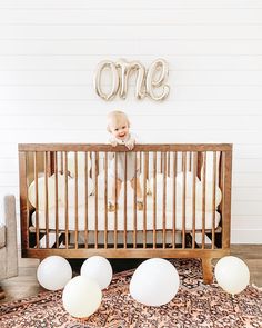 a baby in a crib with balloons and the word one spelled out above it