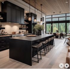 a large kitchen with black cabinets and counter tops next to a dining room table filled with chairs