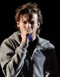 a young man holding a microphone to his mouth while standing in front of a black background