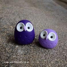 two purple owls with googly eyes sitting on top of a gray rock next to each other