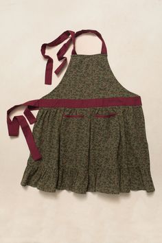 the apron is green with red straps and has a flower pattern on it, as well as a maroon ribbon