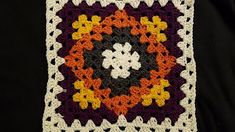 a crocheted square with an orange, yellow and purple flower in the center