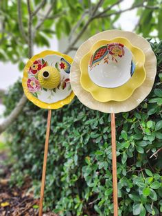 two yellow and white plates sitting on top of each other in front of a bush