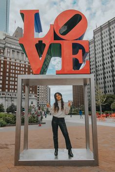 a woman standing in front of a giant love sign with buildings in the back ground