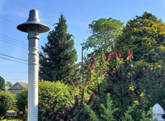 a white lamp post in the middle of a garden with purple flowers and greenery