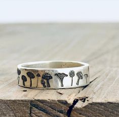 a close up of a silver ring on a wooden surface with trees and mushrooms engraved on it