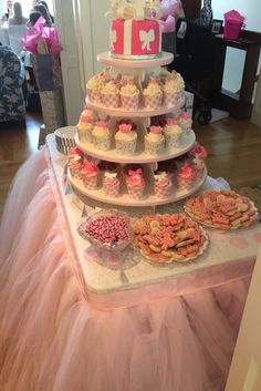 a tiered cake with cupcakes and cookies on the bottom is decorated in pink