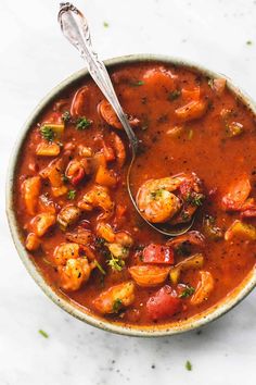 a bowl of shrimp and tomato soup with a spoon in it on a white surface