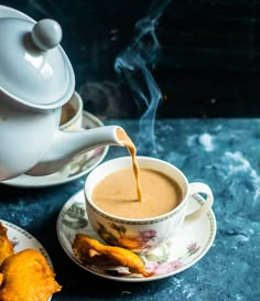 tea being poured into a cup and saucer with pastries on the plate next to it