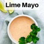 a white bowl filled with cilantro lime mayo next to a slice of lime