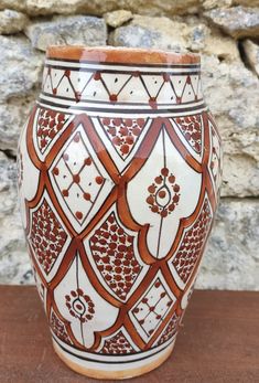 a brown and white vase sitting on top of a table next to a stone wall