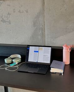 an open laptop computer sitting on top of a desk next to ear buds and headphones