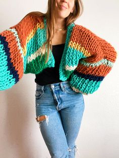 a woman in ripped jeans and a multicolored sweater is posing for the camera