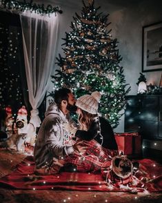 a man and woman sitting on the floor next to a christmas tree with their dog