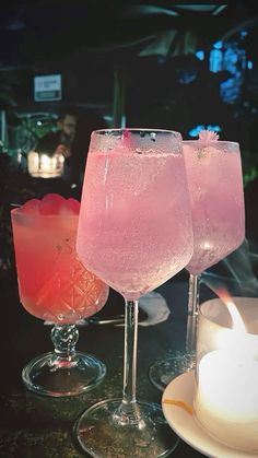 two glasses filled with pink liquid sitting on top of a table next to a candle