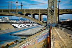 a train traveling under a bridge next to a river filled with lots of power lines