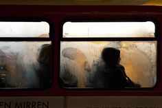 two people are seen through the window of a public transit bus on a rainy day