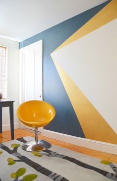 a yellow chair sitting on top of a wooden floor next to a wall painted in blue and gold