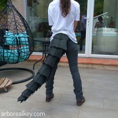 a woman in white shirt and grey pants with black feathers on her legs standing next to a hammock