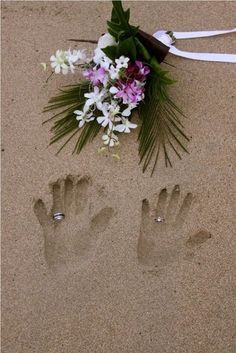 an image of someone's hand and foot prints in the sand with flowers on it