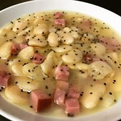 a white bowl filled with ham and dumplings in gravy on top of a table