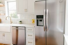 a stainless steel refrigerator and sink in a kitchen with white cabinets, wood flooring and wooden floors