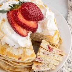 a white plate topped with pancakes covered in whipped cream and sliced strawberries on top