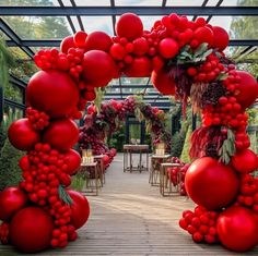 an archway made out of red balloons and greenery in a garden setting with tables and chairs