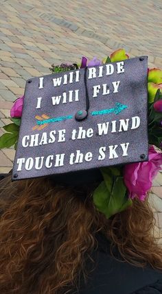 a woman wearing a graduation cap with flowers on her head and writing on the side