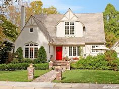 a white house with a red door in the front yard and green grass around it