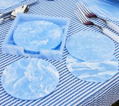 blue plates and forks are sitting on a striped tablecloth with white napkins that have been folded over them