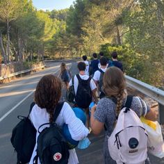 a group of people with backpacks walking down a road in front of some trees