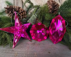 three pink christmas ornaments hanging from evergreen branches