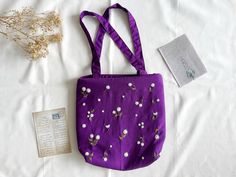 a purple bag with white flowers on it next to a card and some dried plants