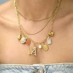 a close up of a person wearing a necklace with charms on it and an initial