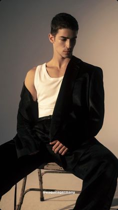 a young man sitting on top of a chair wearing a black suit and white shirt