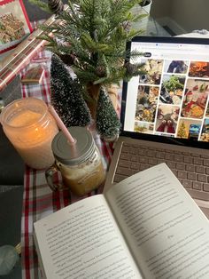 an open book sitting on top of a table next to a laptop computer and candle