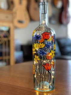 a glass bottle with flowers painted on it sitting on a wooden table in front of a guitar