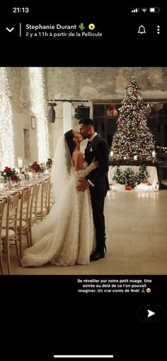 a man and woman are kissing in front of a christmas tree with lights on it