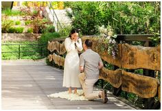 a man kneeling down next to a woman on a wooden bridge while talking on a cell phone