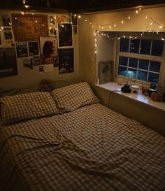 an unmade bed in a dorm room with lights strung from the ceiling and posters on the wall