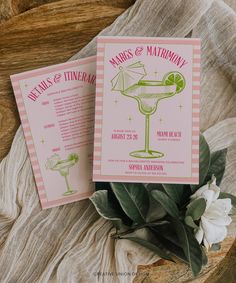 two pink and green cocktail menus sitting on top of a wooden table next to flowers