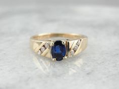 Simple, refined and set low to the hand, this vintage sapphire ring would make a great piece for day to day wear. The stone has plenty of shine and a rich color, accented by the simply set diamond shoulders.Metal: 14K Yellow GoldGem: Sapphire .48 CaratGem Measurements: 4 x 5.8 mm, Oval Accent: 6 Diamonds .18 CaratRing Size: 4.75Marks: "O14KT<>61B"Stamped on the inside band SKU: 65UE3E-DEach piece has been identified and graded by a Graduate Gemologist who has been certified by the Gemologi Classic Blue Diamond Ring With Accents, Classic Sapphire-colored Diamond Ring With Center Stone, Classic Blue Sapphire Ring With Diamond Accents, Classic Sapphire Birthstone Ring, Classic Sapphire Halo Ring, Classic Oval Ring With Channel Set, Classic Sapphire Birthstone Ring With Gemstone, Classic Oval Channel Set Ring, Classic Sapphire Ring With Diamond