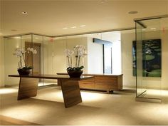 an empty room with glass walls and flowers in vases on the table, surrounded by large mirrors