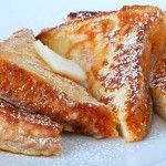 two pieces of french toast on a white plate with powdered sugar and butter sprinkled on top