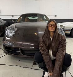 a woman sitting on the ground in front of two porsches with their hood up