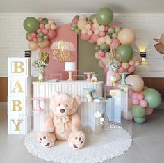 a teddy bear sitting on the floor in front of a baby shower sign and balloons